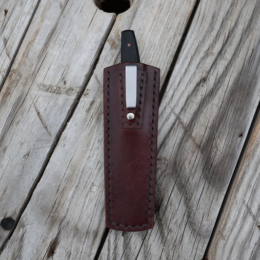 Brown leather knife sheath with a silver clip on a wooden surface