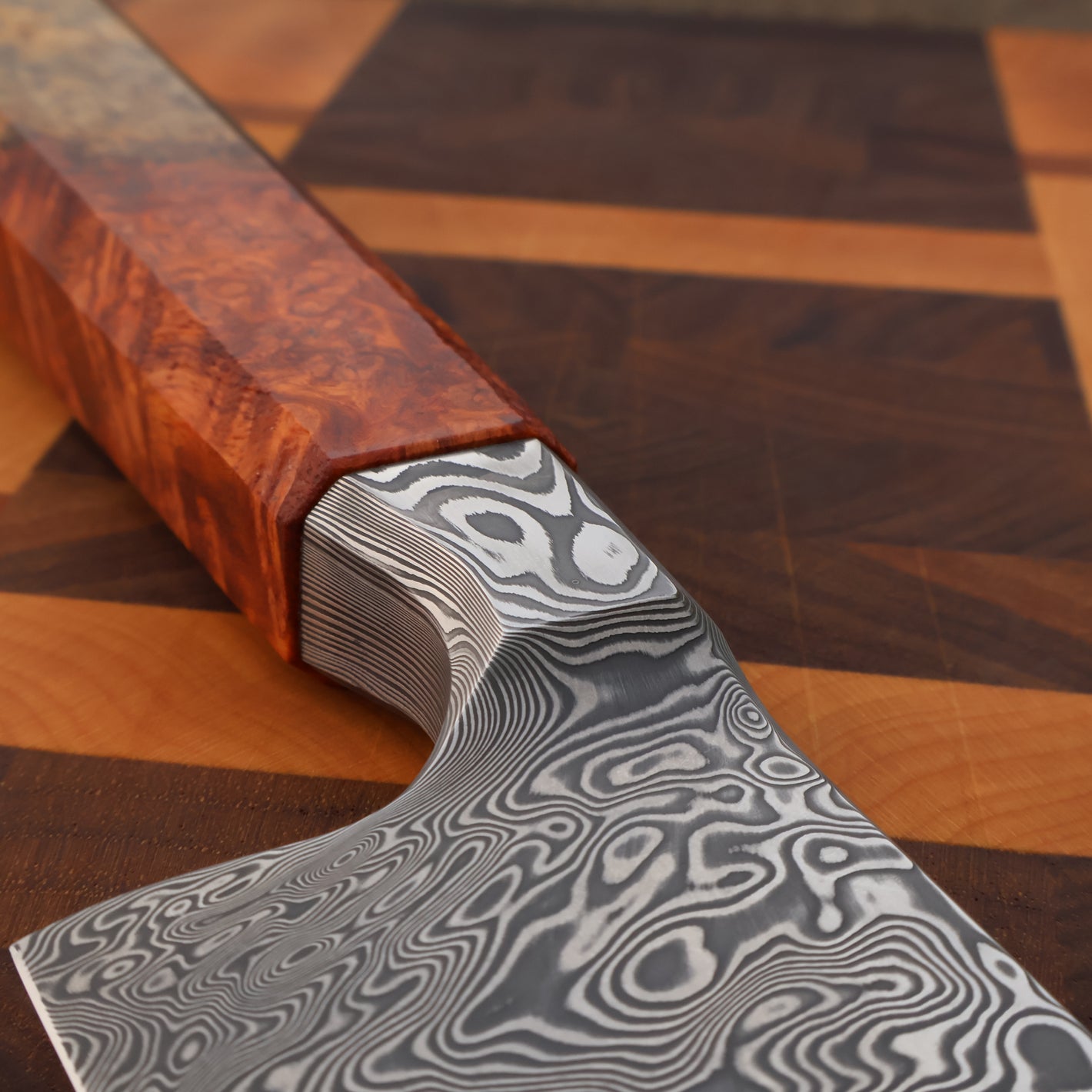 Close-up of a knife with a wooden handle and patterned metal blade on a wooden surface.