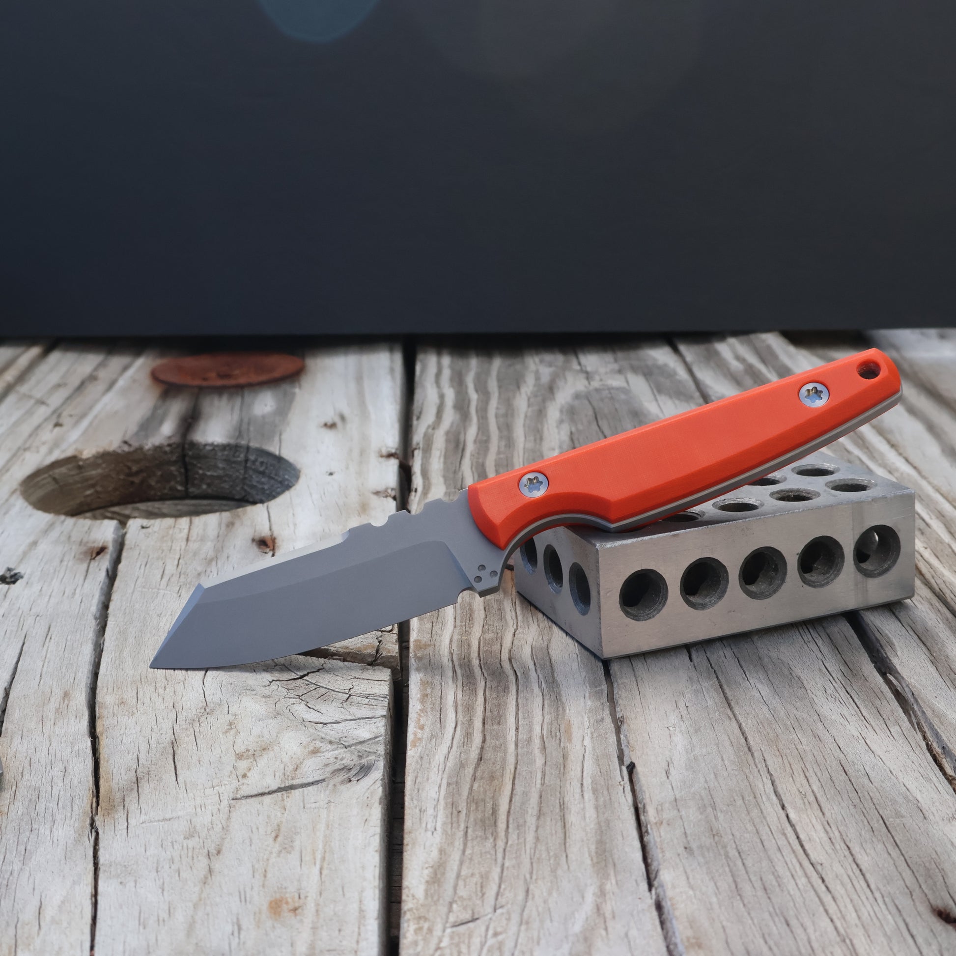 fixed blade knife with bright orange handle resting on a metal block 
