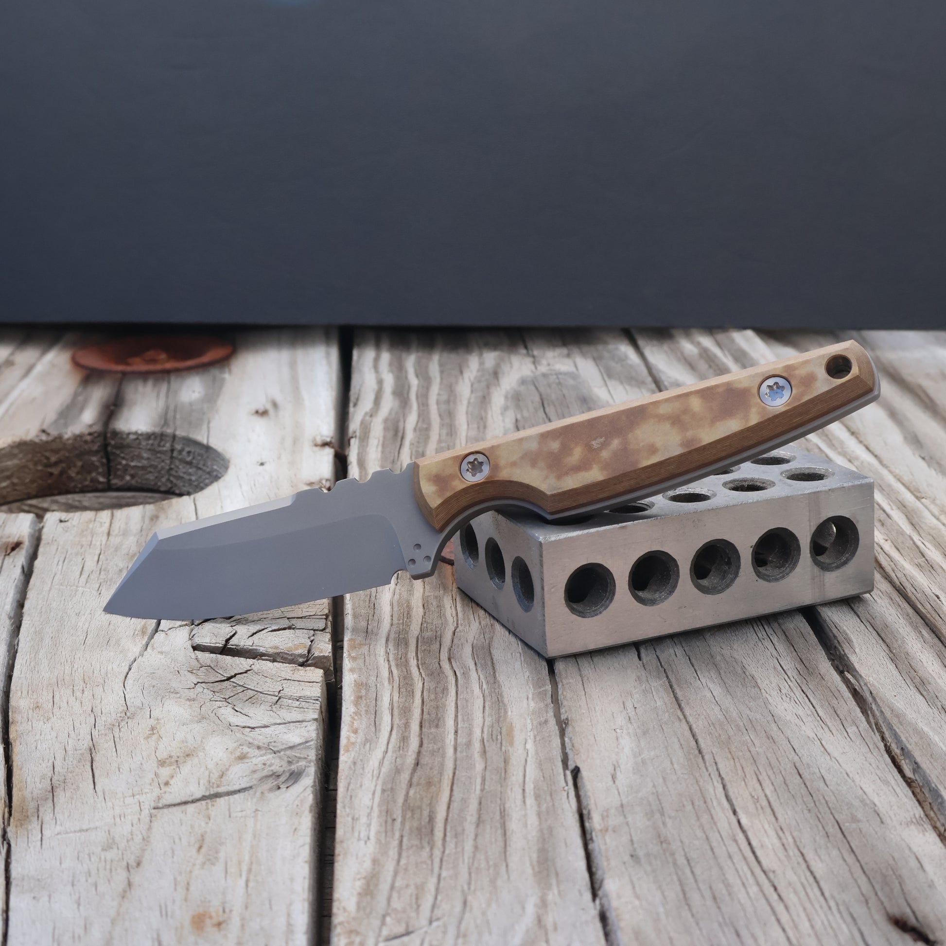 fixed blade knife with mulitcolor tan handle resting on a metal block