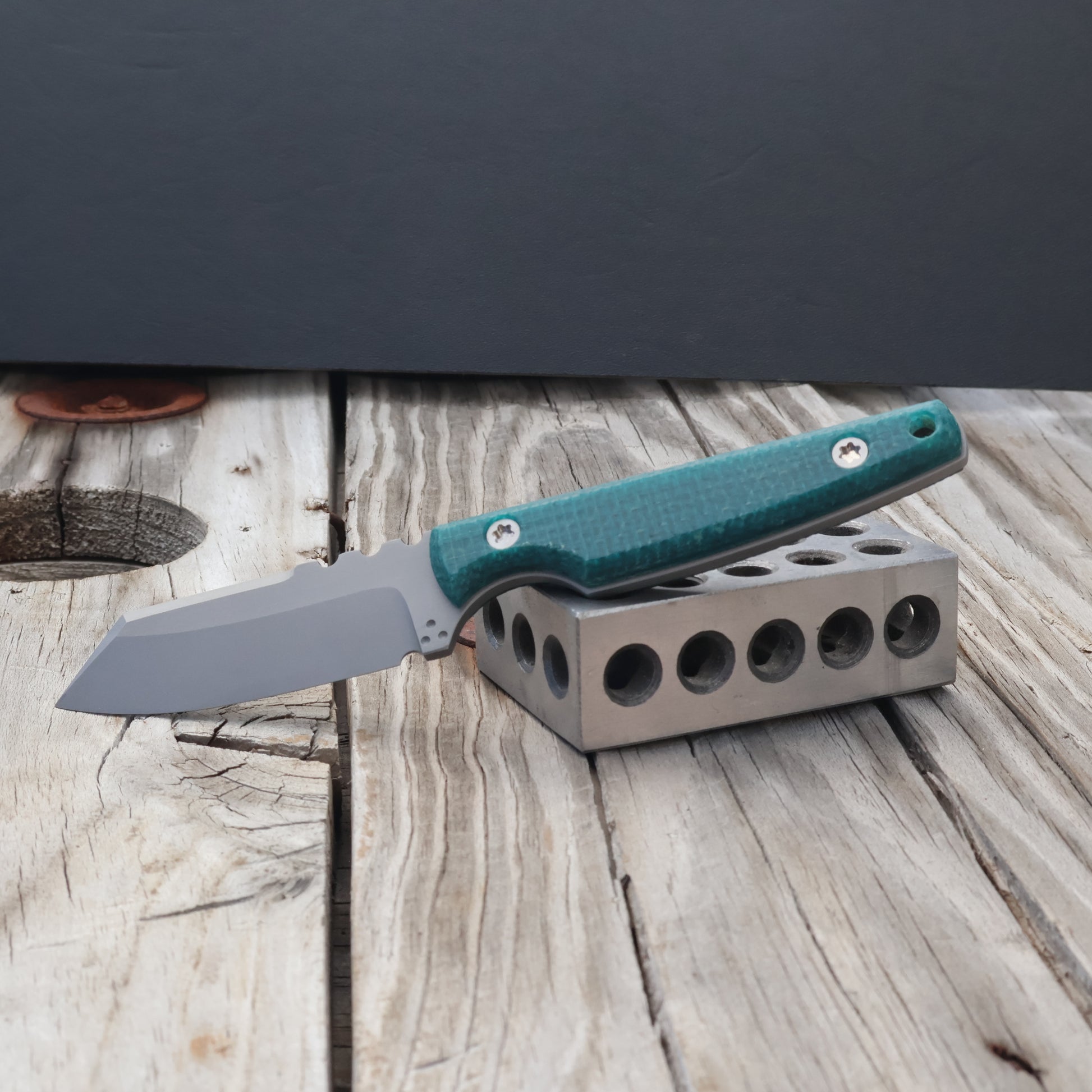fixed blade with emerald burlap micarta handle sitting on a metal block