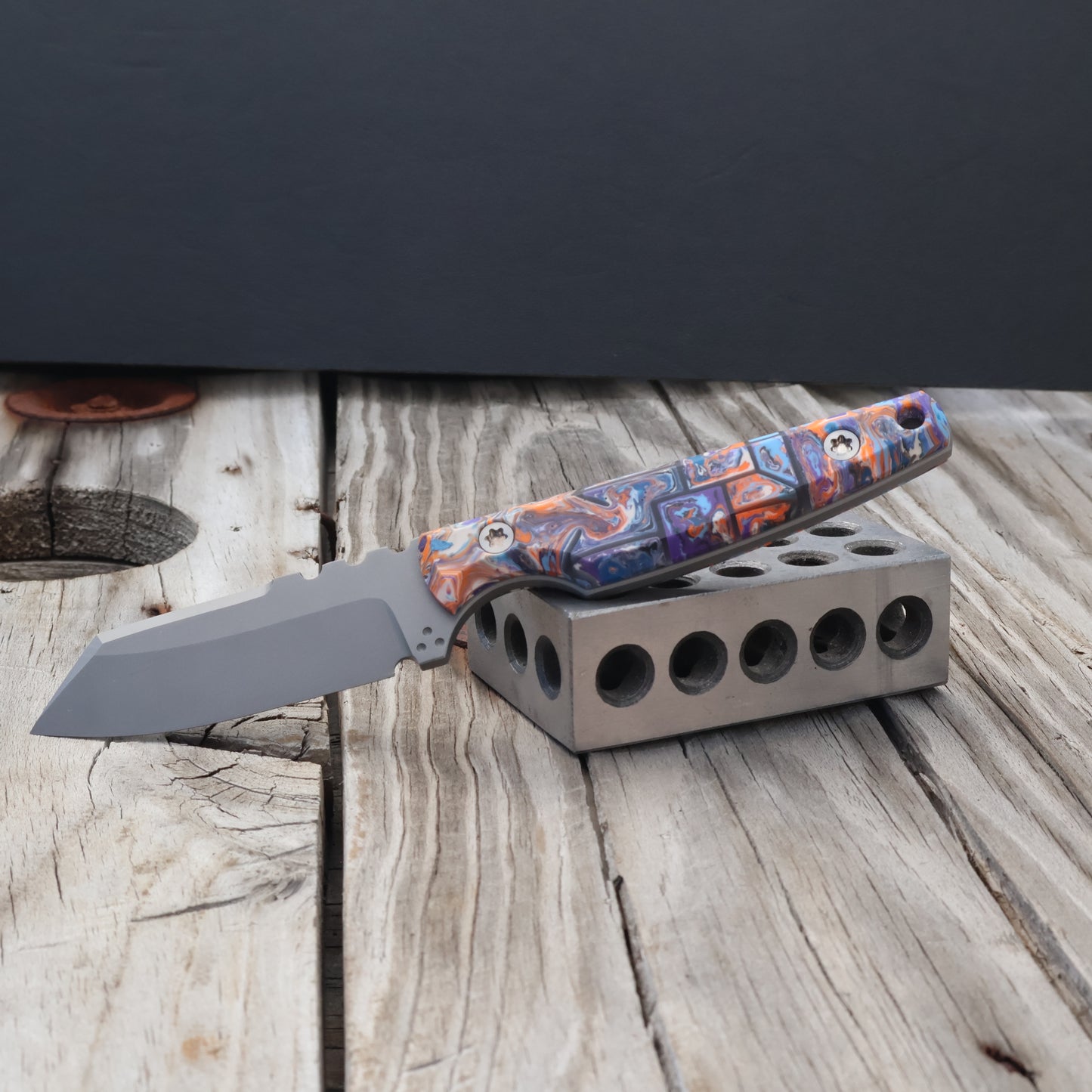 fixed blade knife with colorful resin handle sitting on a metal 123 block 