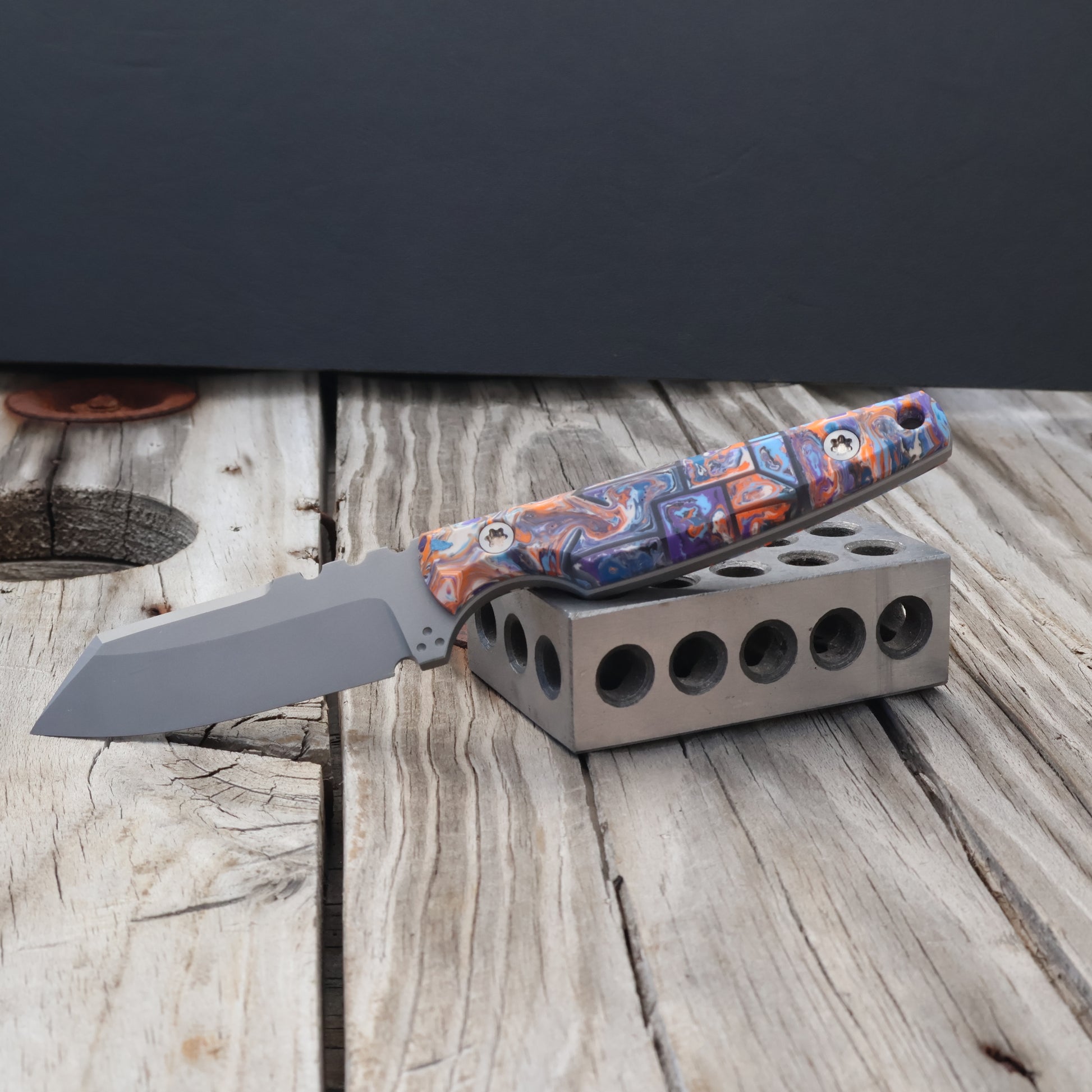fixed blade knife with colorful resin handle sitting on a metal 123 block 