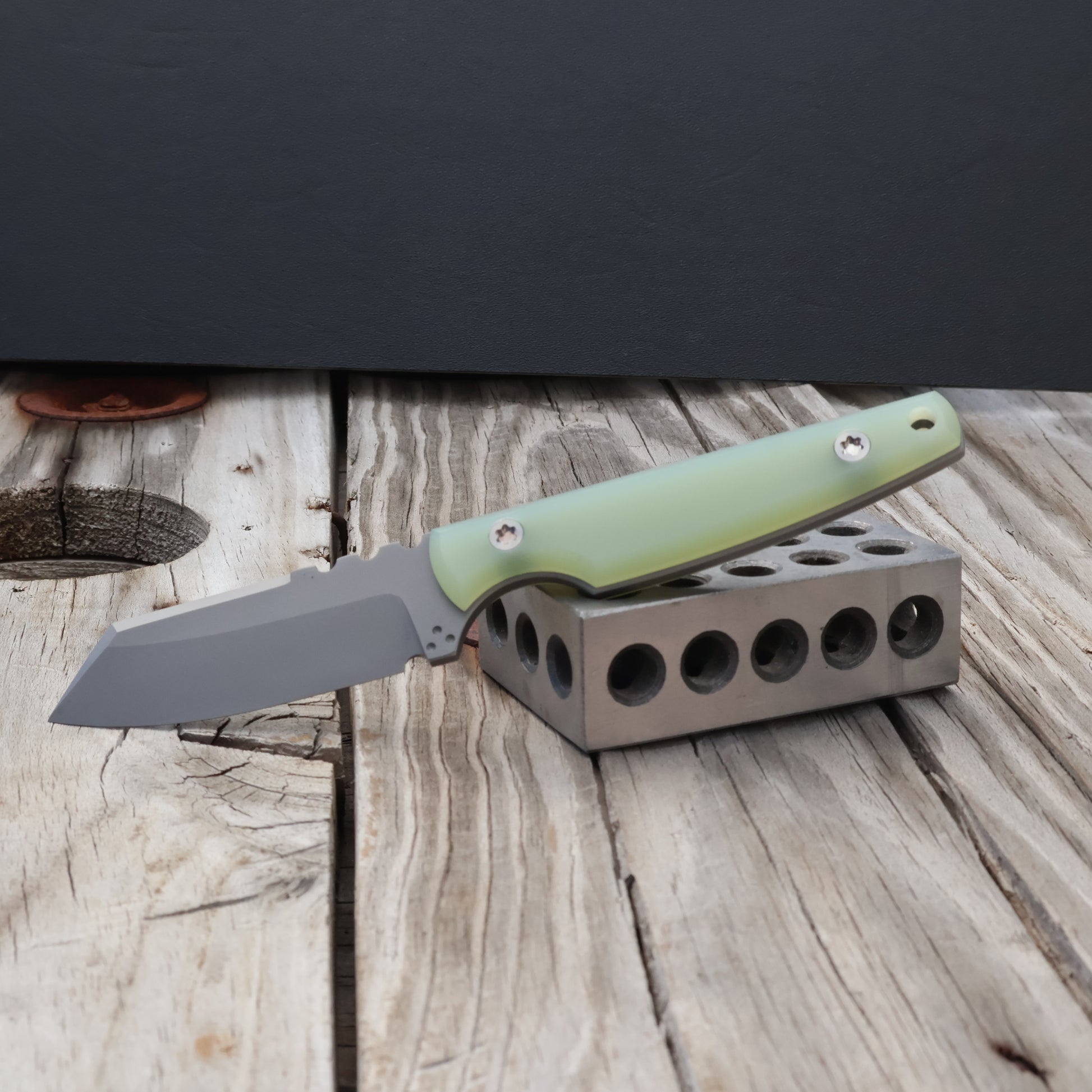 fixed blade knife with jade colored handle sitting on a metal block