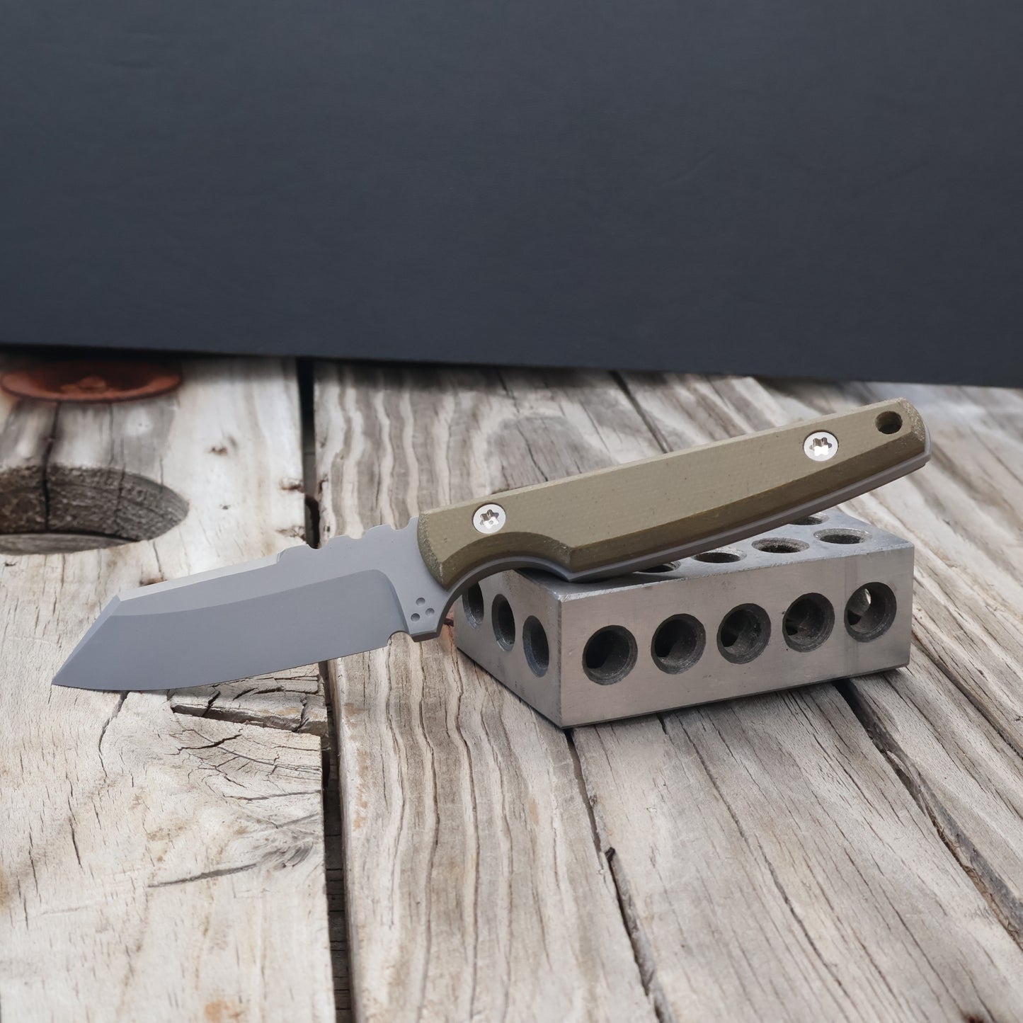 fixed blade knife with OD green handle resting on metal block with black background