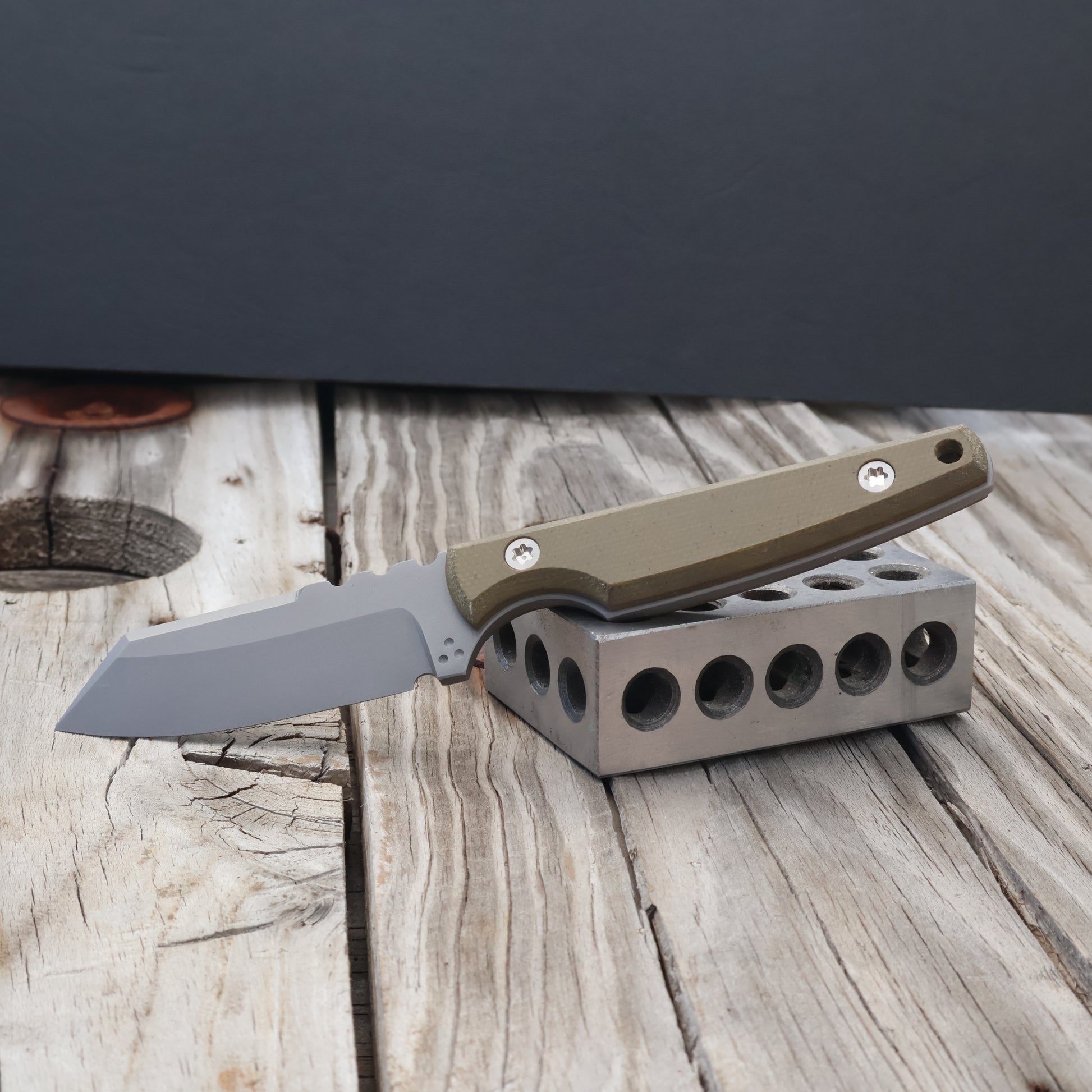 fixed blade knife with OD green handle resting on metal block with black background