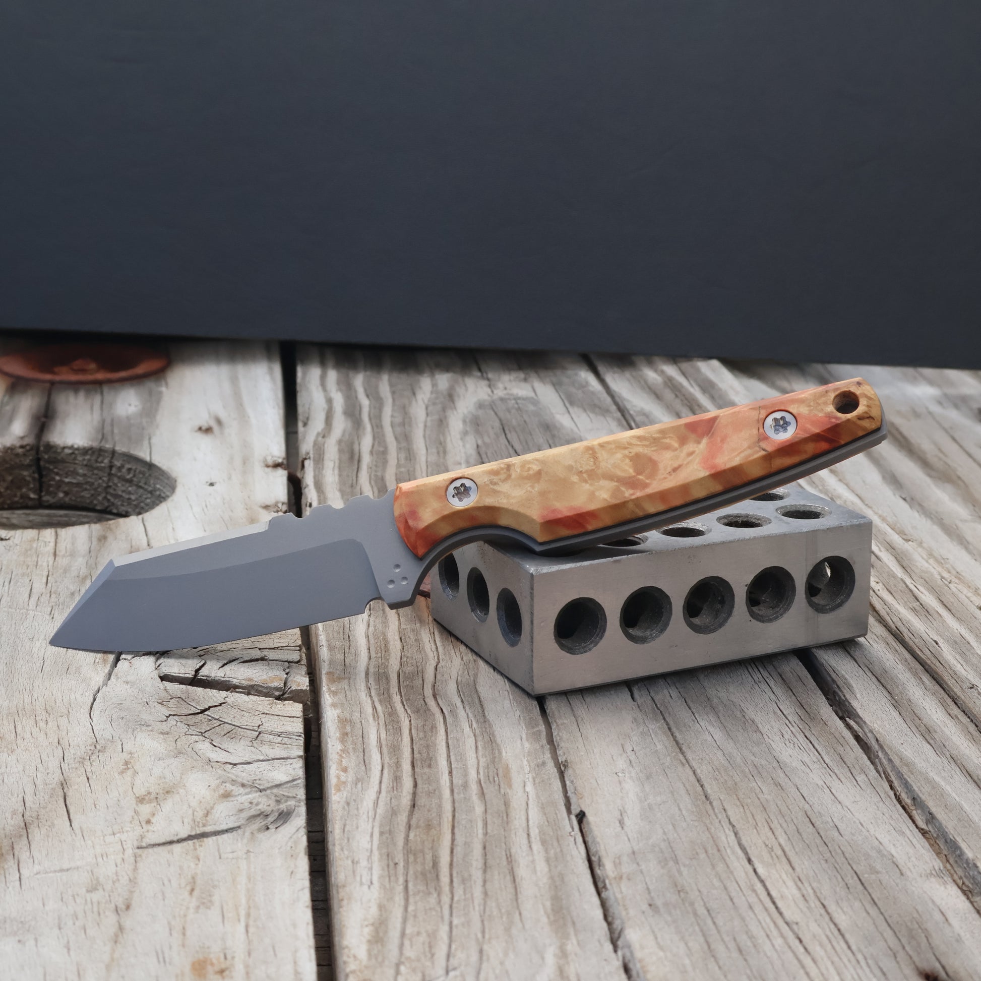 fixed blade knife with light and rose colored wood handle resting on metal block 