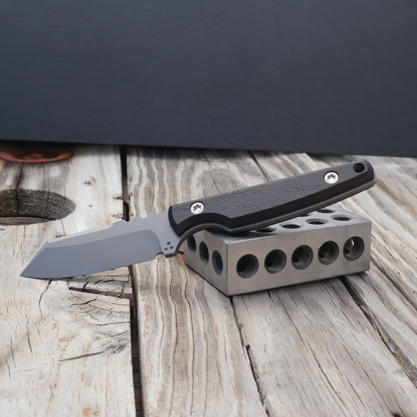 fixed blade knife with black bog oak handle resting on metal block with black background