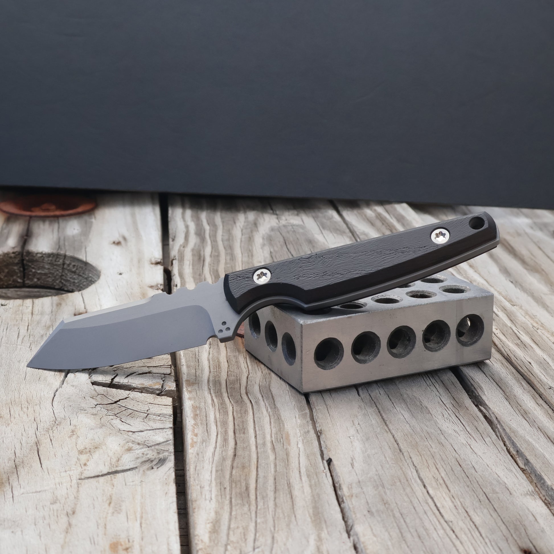 fixed blade knife with black bog oak handle resting on metal block with black background