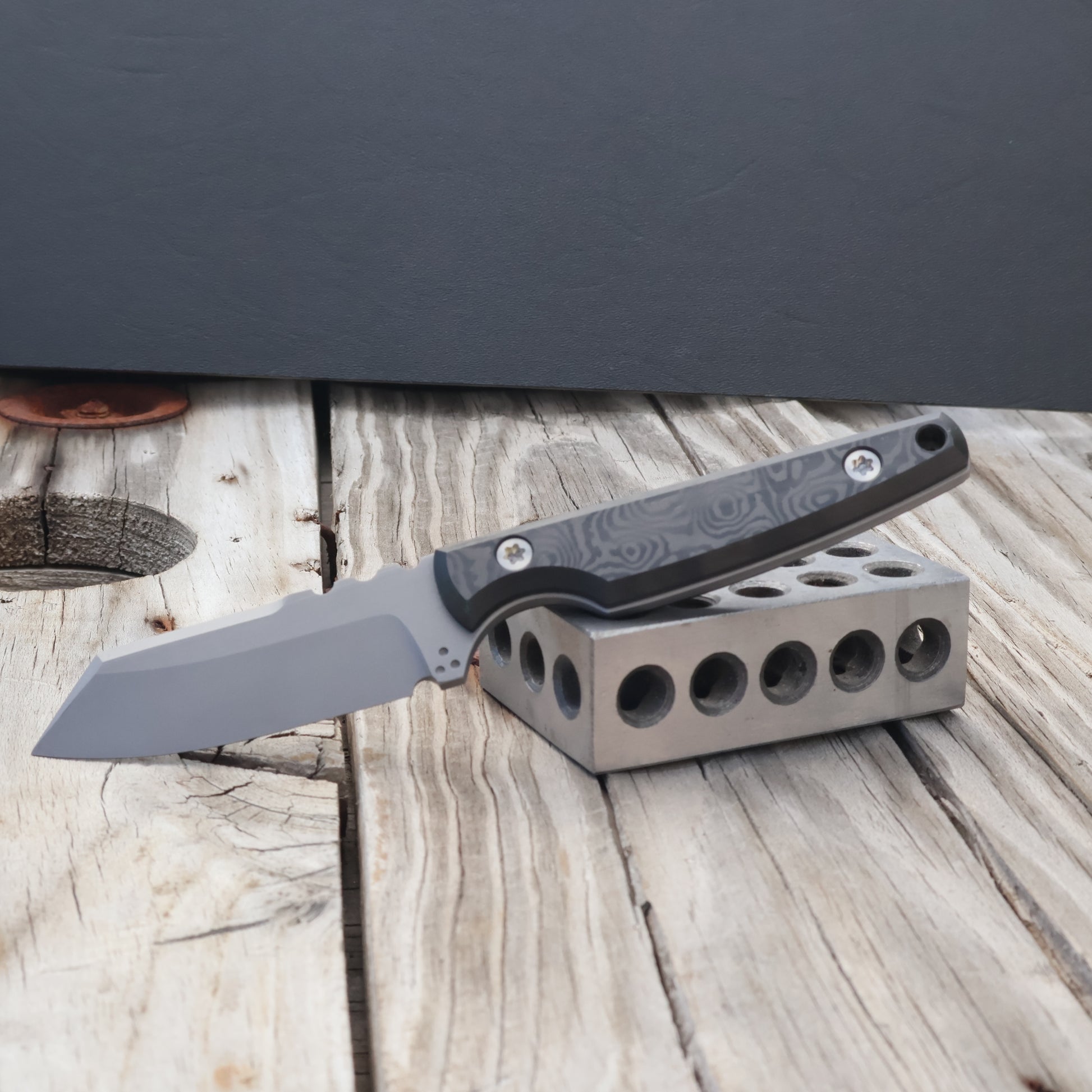 fixed blade knife with topographic carbon fiber handle resting on metal block 