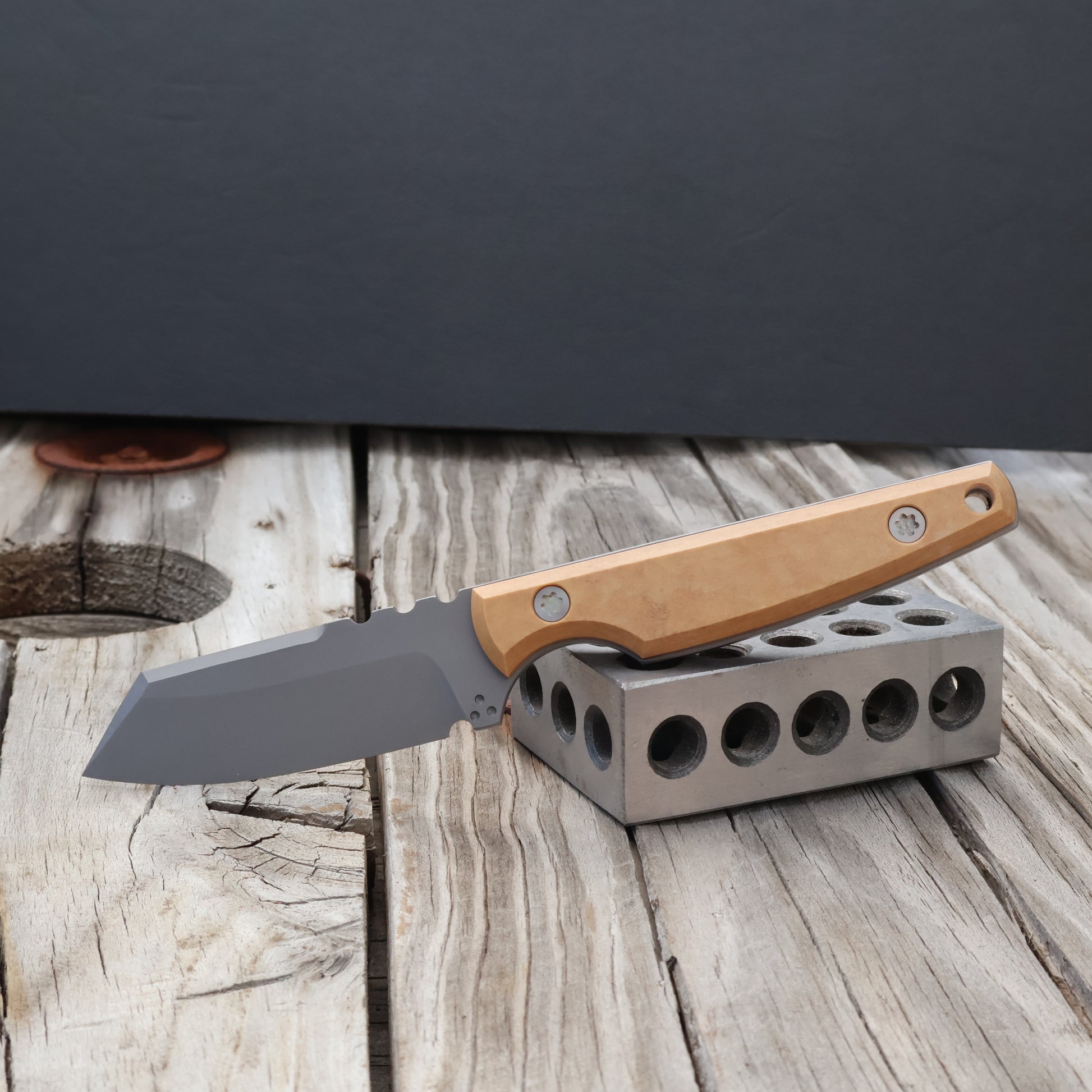 Knife with a tan richlite handle on a metal stand against a dark background