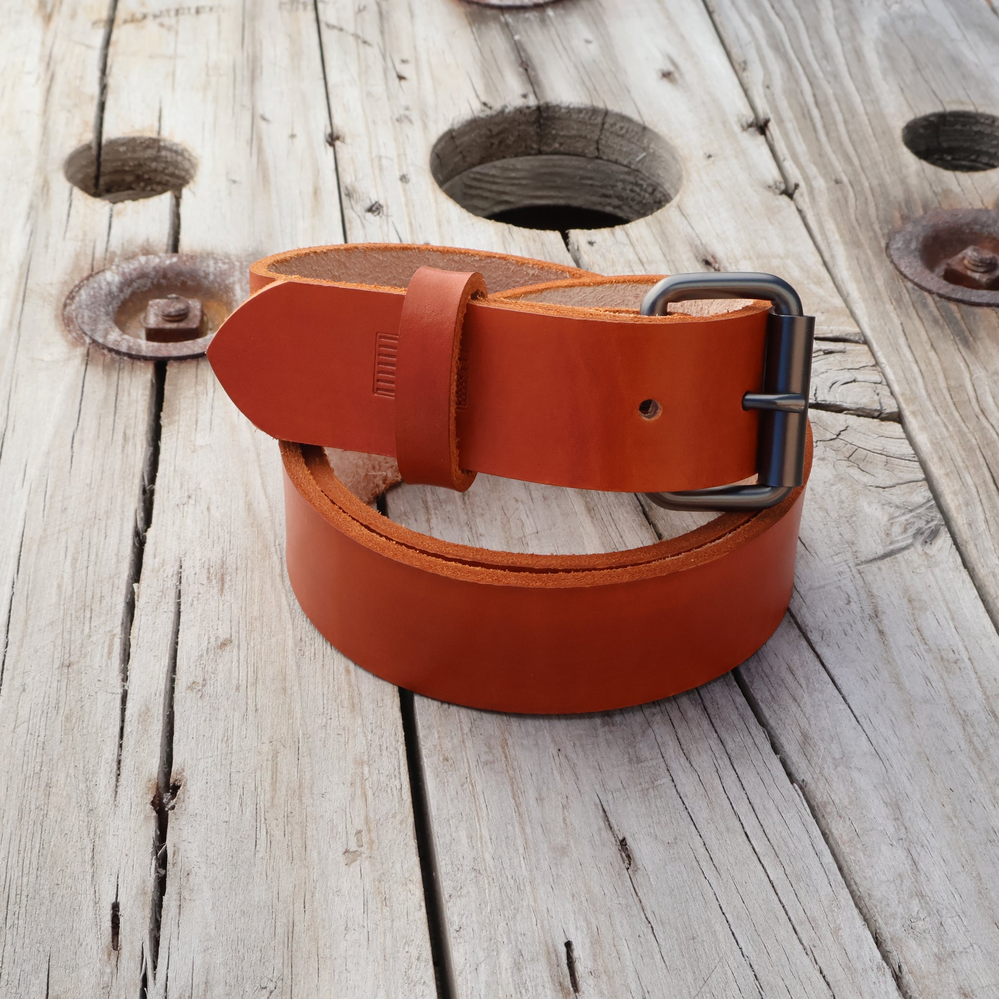 Saddle tan leather belt with black buckle on a wooden surface