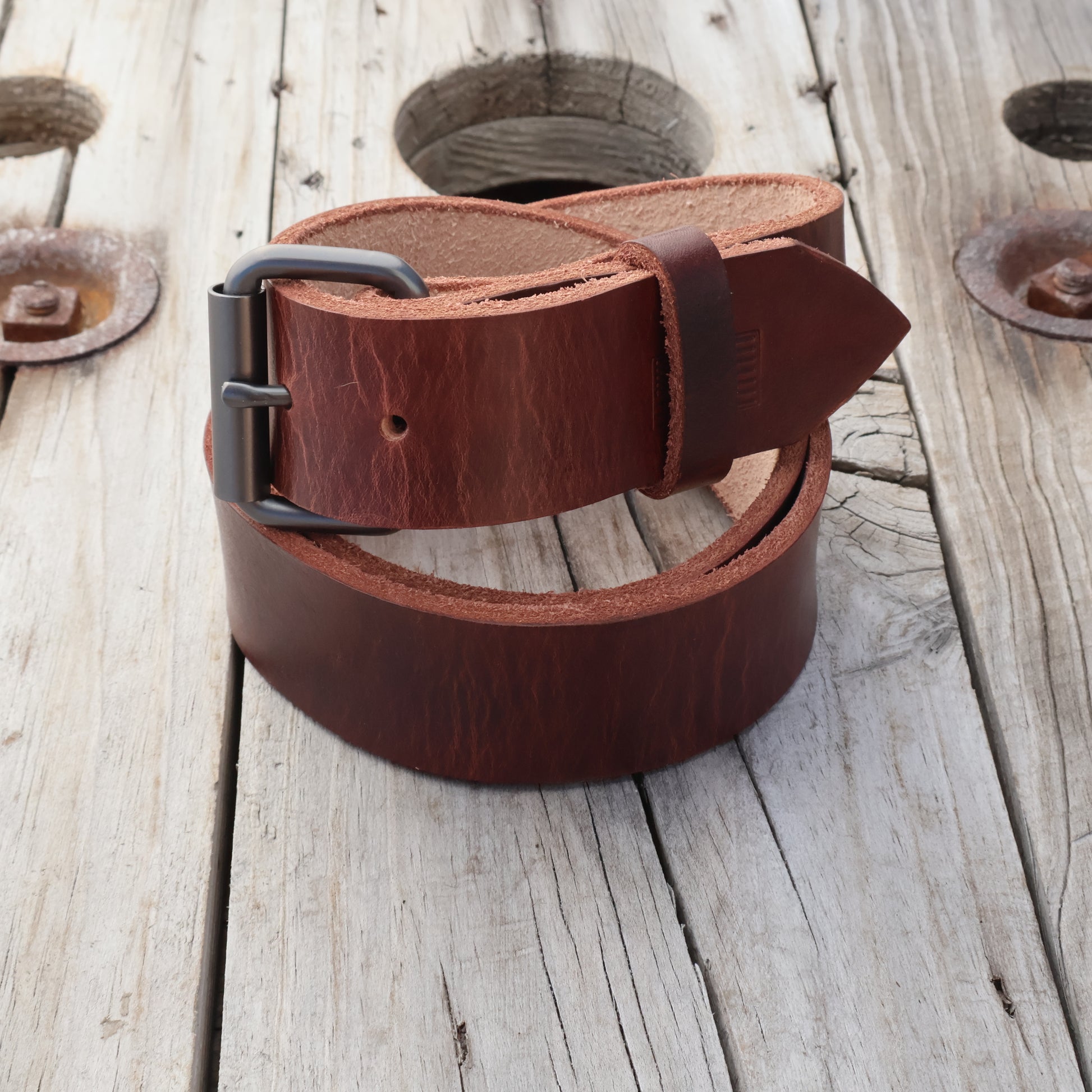 Brown leather belt with a black buckle on a wooden surface