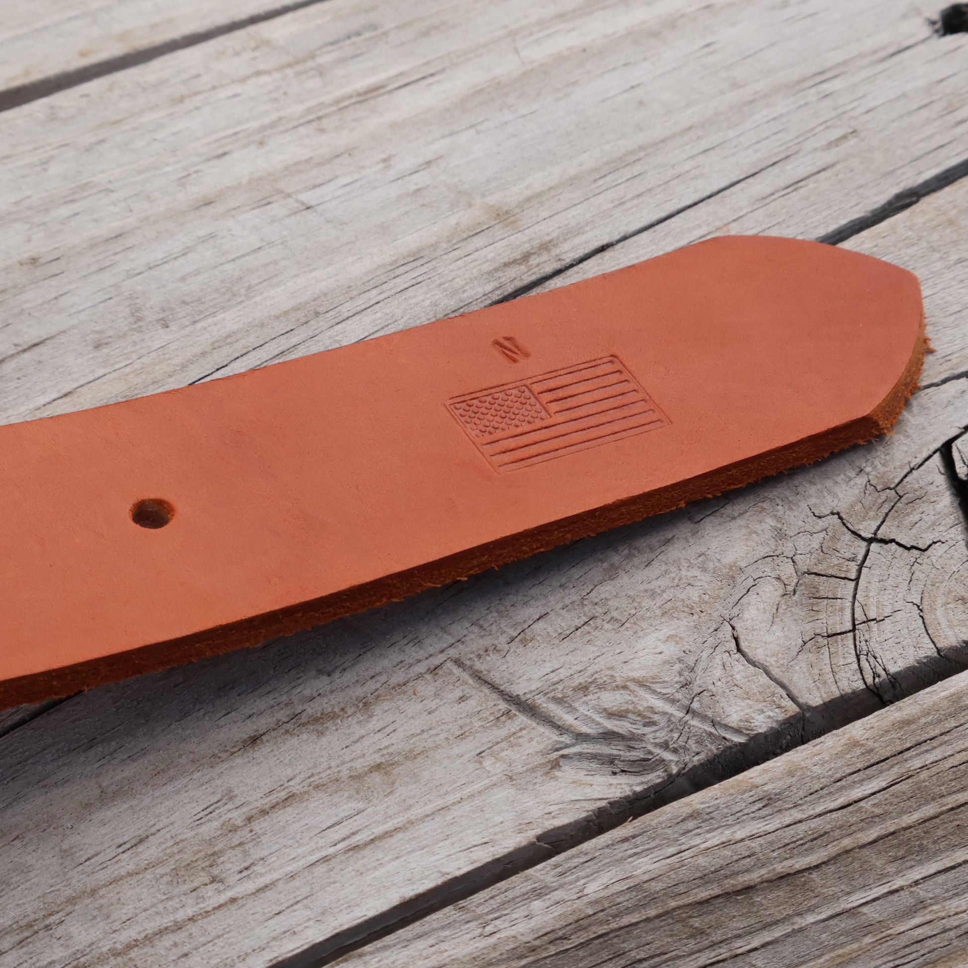 Brown leather belt with an American flag embossing on a wooden surface