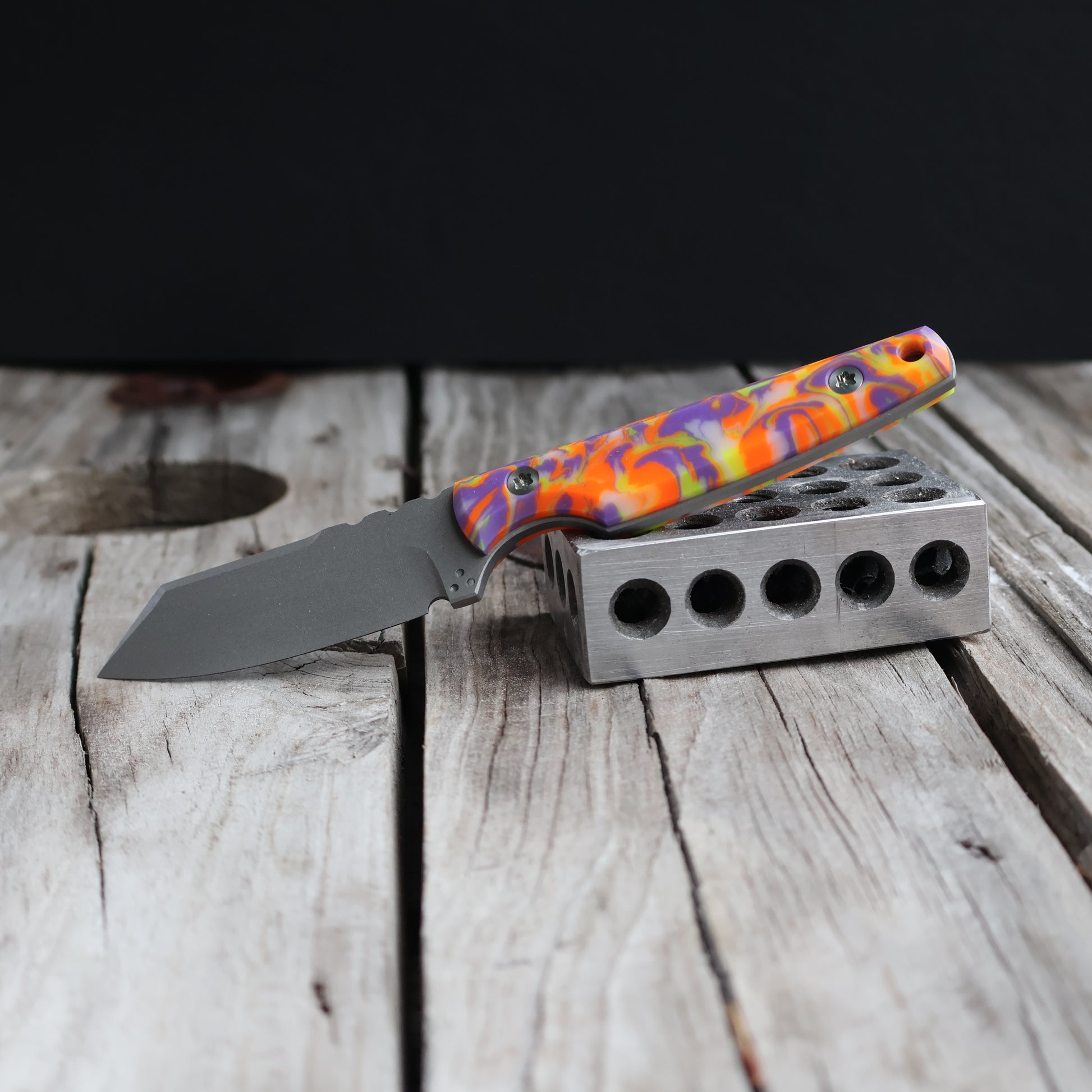 fixed blade knife with brightly colored handle resting on metal block