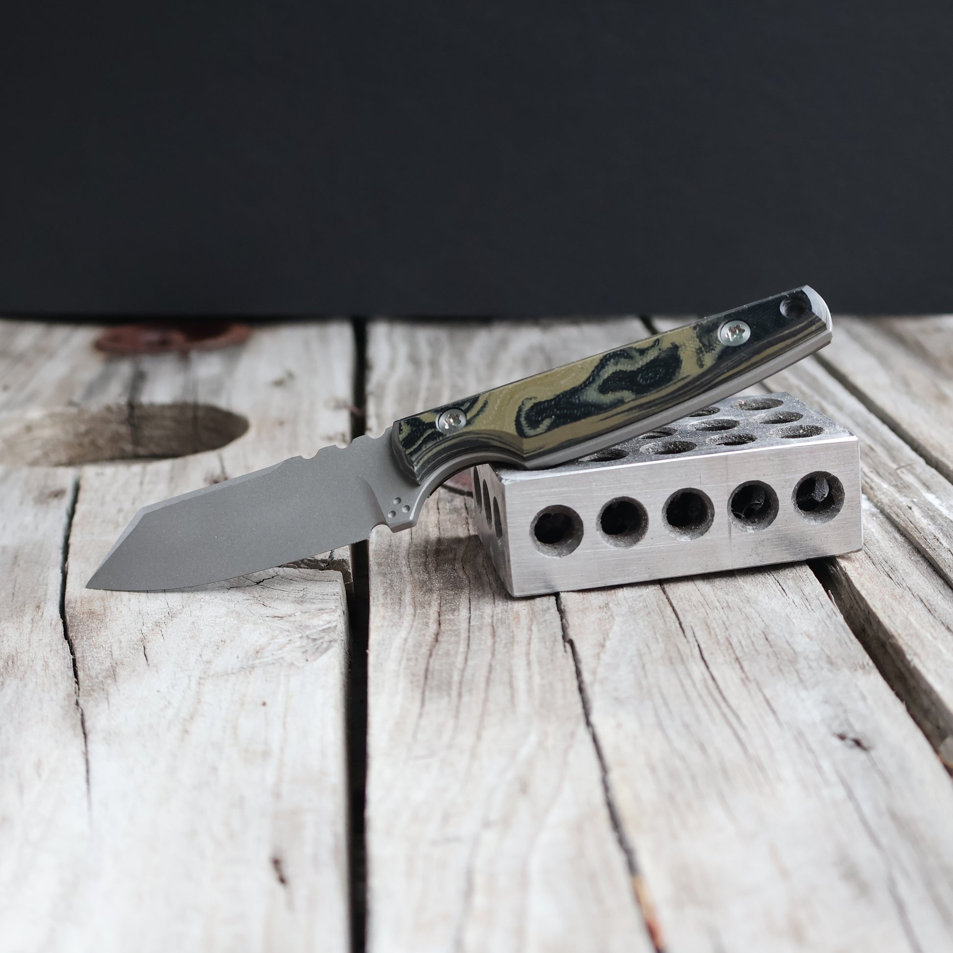 fixed blade knife with green and black handle propped on metal block 