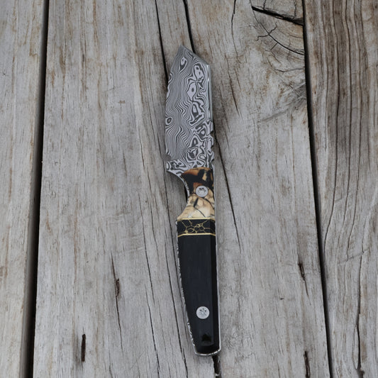 Decorative knife with a black handle and patterned blade on a wooden surface