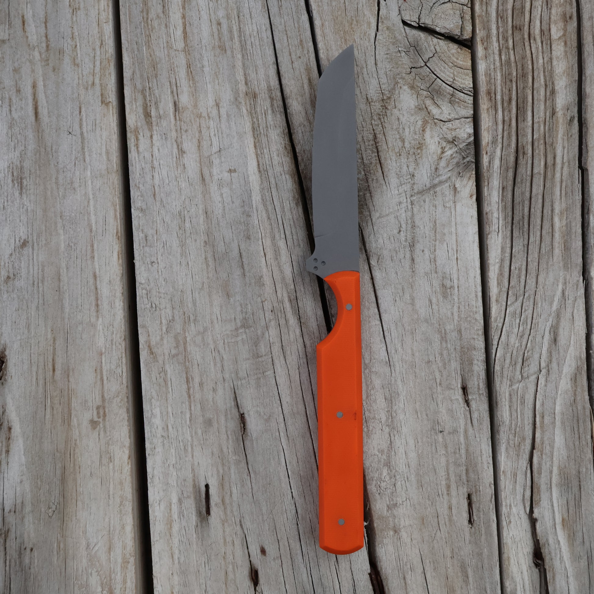 Orange handled knife with a gray blade on a wooden surface