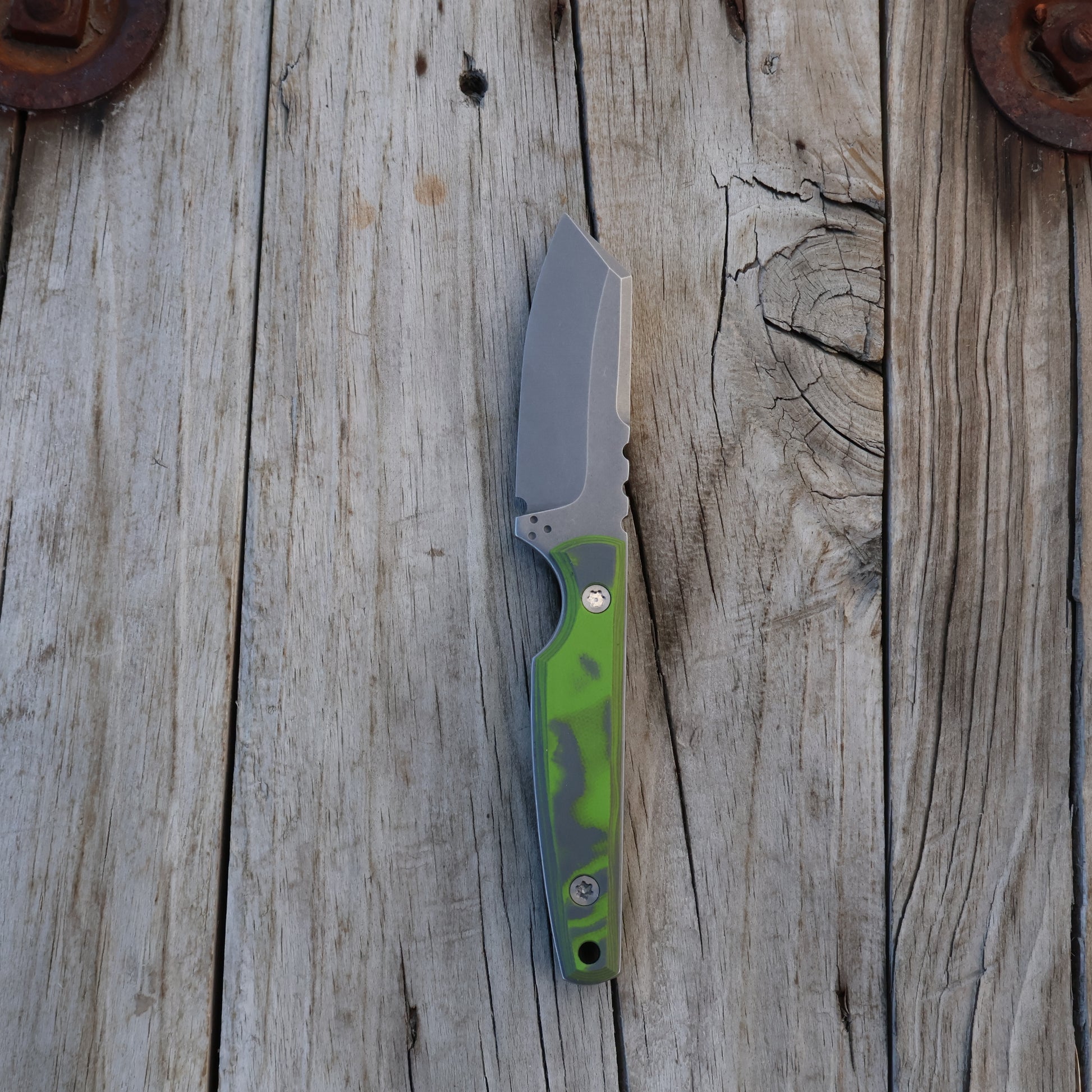 fixed blade knife with a green and gray handle on a wooden surface