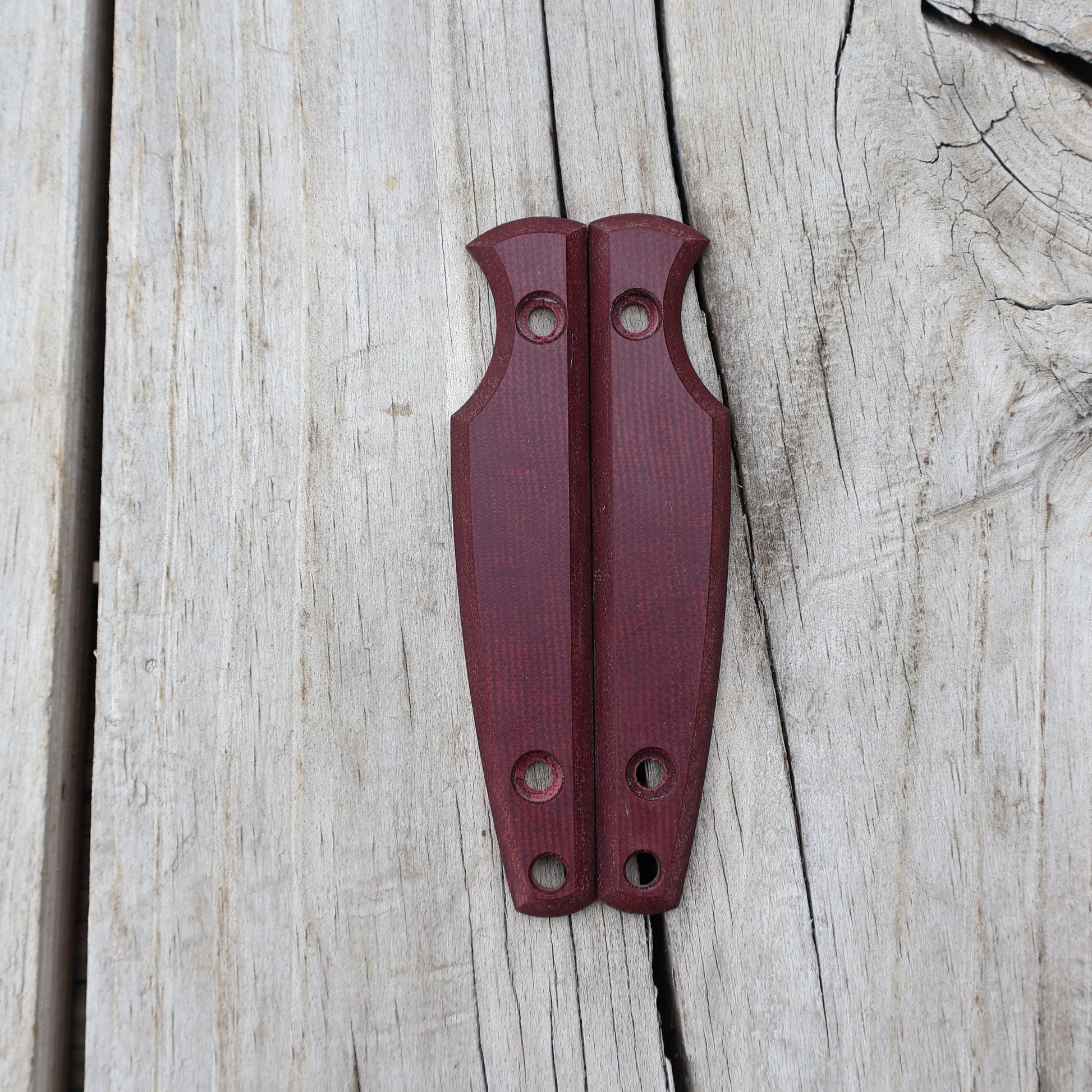 Pair of burgandy knife handle scales on wooden surface 