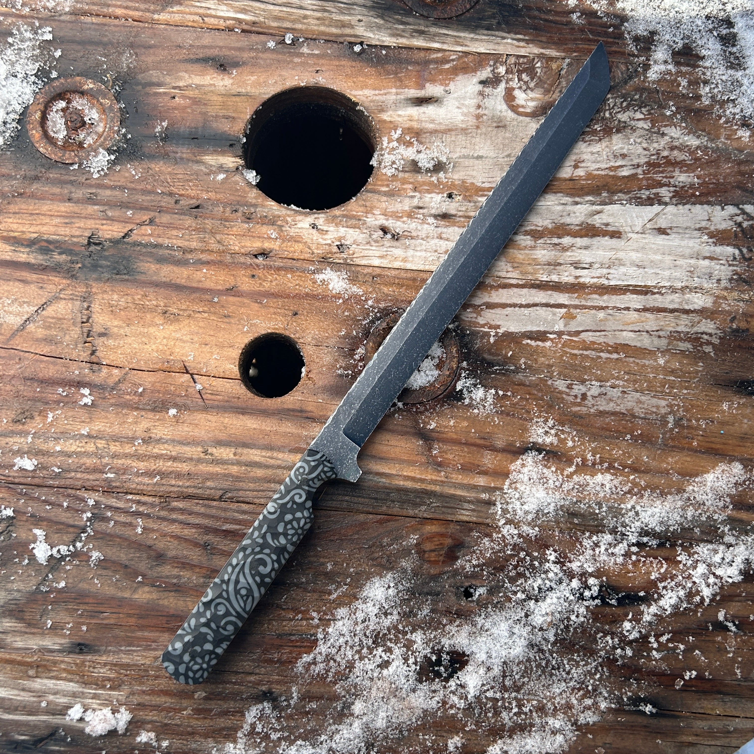 short sword with black handle and blade on snow covered wood surface 