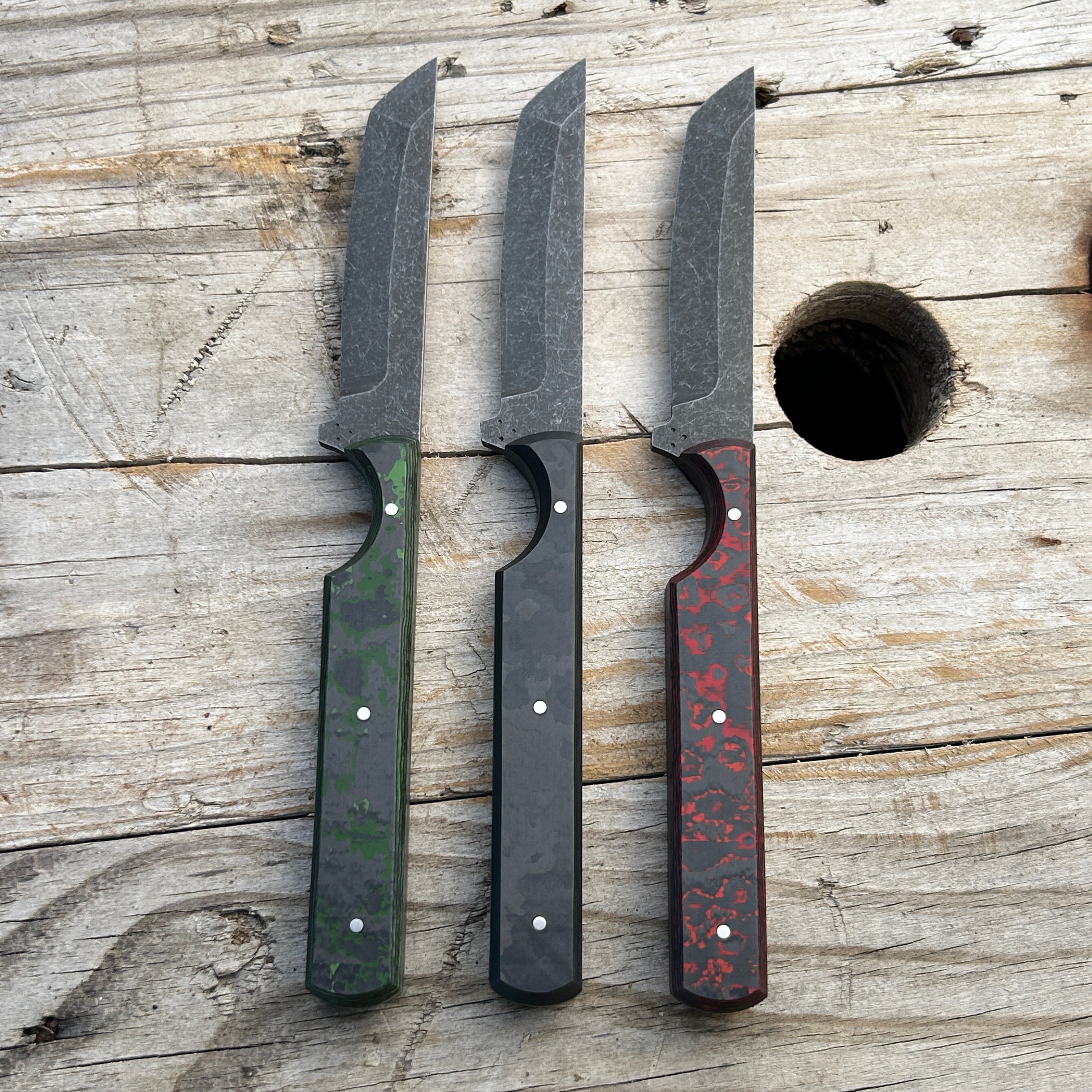 three tanto fixed blade knives with different colored handles sitting on wooden surface 