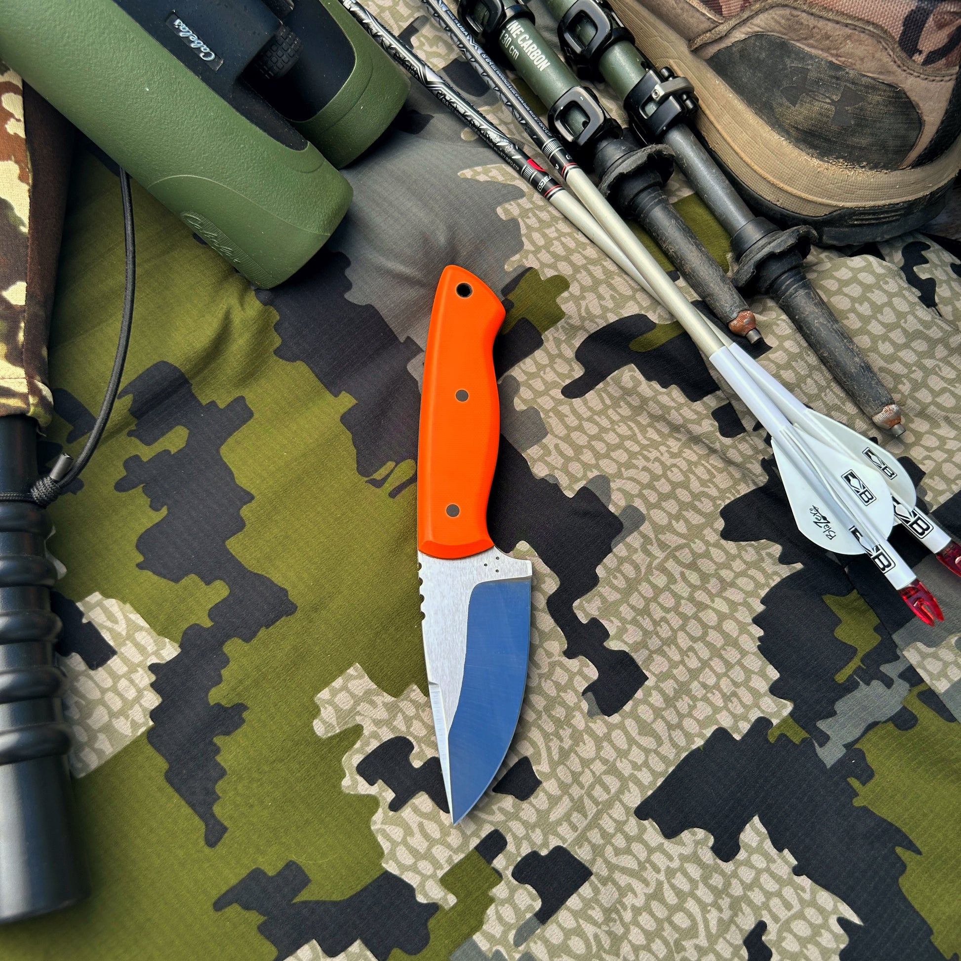 Orange handled drop point hunter knife pictured with hunting gear. Great gift for any outdoorsman 