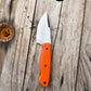 Profile view of orange handled drop point knife pictured on weathered wood backdrop. Great camping and hunting knife with bright orange handle that is easy to spot in the woods so you won't lose it.