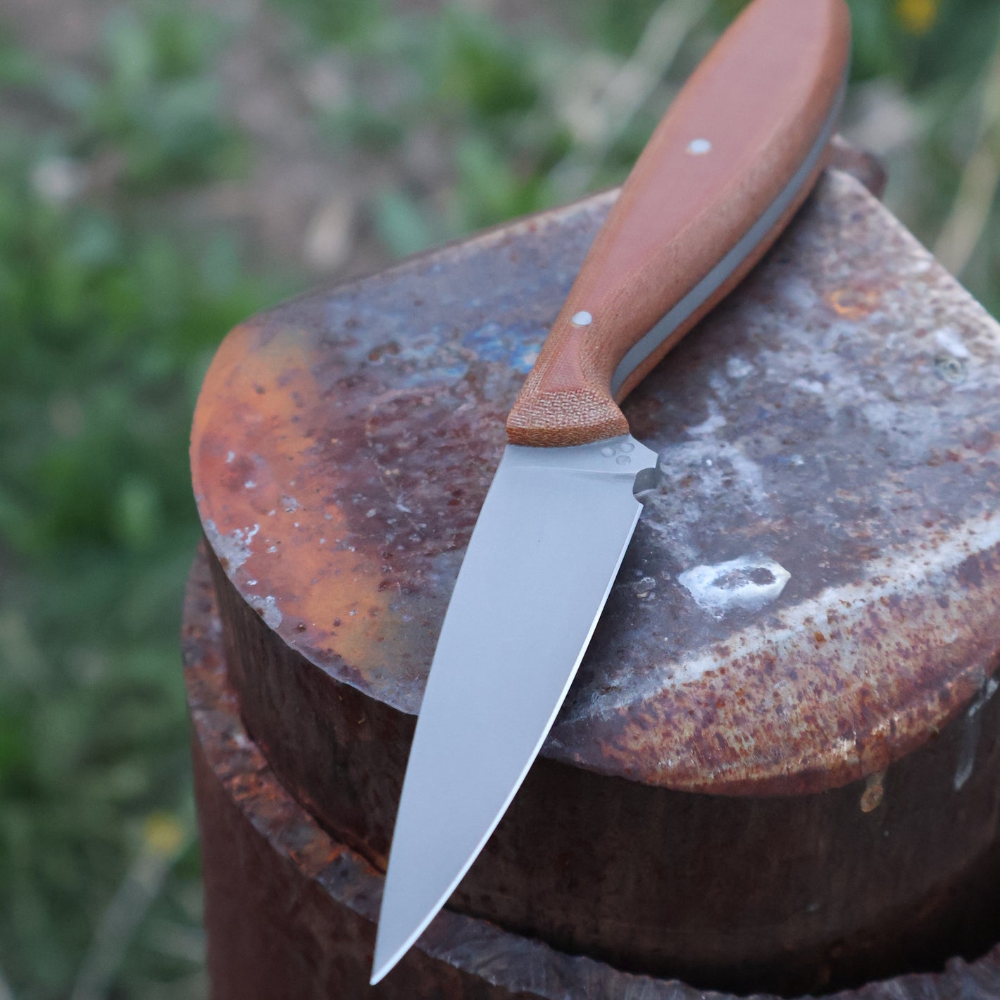 Knife with a brown handle on a rusty metal surface outdoors