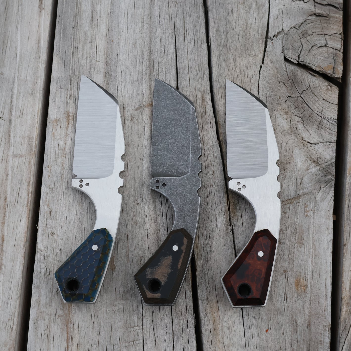 Three small knives with different blade handles on a wooden surface