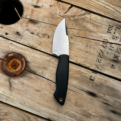Top down shot of the profile of the black handled Colorado Hunter knife on a weathered wood background. The profile of the knife is a classic drop point style. It has an approx 3.5" blade & is approx 8.25" long. The handle is slightly curved to fit comfortably into the hand and has a swell in the middle to provide good ergonomics for all day use. 